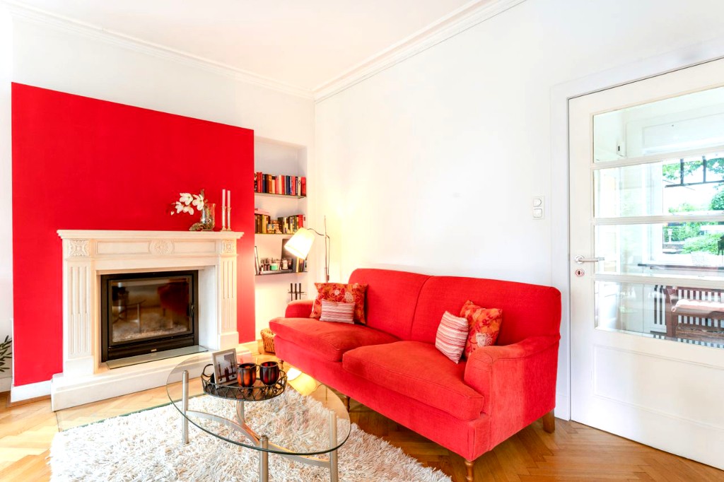 Helles Wohnzimmer mit rotem Sofa, Kamin, roter Akzentwand und Parkettboden